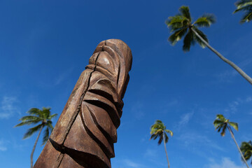 Wood carved tiki under a blue sky and palm trees on a French Polynesia tropical island