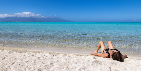 Woman laying down on sandy beach on a tropical island to sunbathe near clear turquoise water