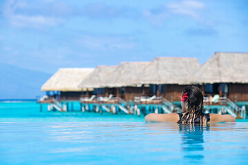 Beautiful woman on vacation at a tropical island resort swimming near overwater bungalows in a blue infinity pool overlooking the ocean