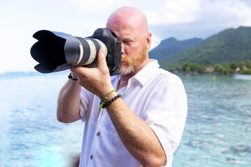 Professional photographer holds camera with long lens taking a picture on a tropical island