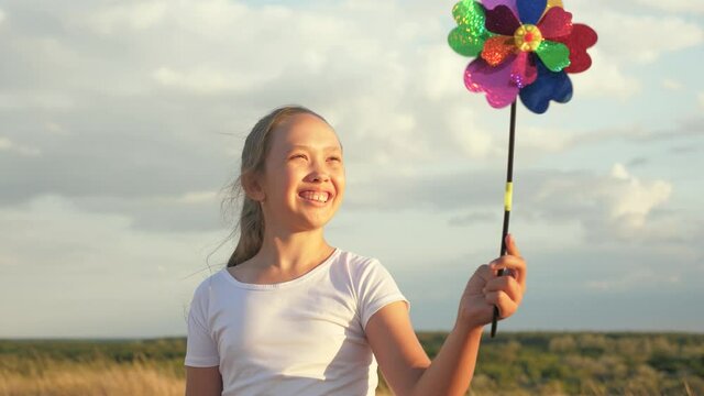 girl playing pinwheel park in slow motion. Happy child playing having fun pinwheel. Happiness vacation childhood children happy family holiday. childhood concept. child playing in park catches wind