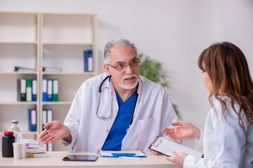 Fototapeta premium Old male doctor and his young female assistant in the clinic
