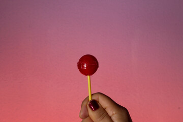 paleta de dulce roja sujetada con una mano en fondo rosa 