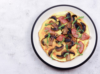 Omelet with mushrooms, cheese and sausages on a round plate on a light gray background. Top view, flat lay