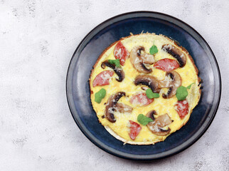 Omelet with champignons, cheese and sausages on a round plate on a light gray background. Top view, flat lay