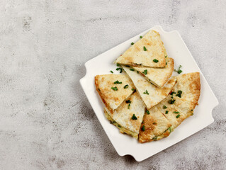 Breakfast quesadilla with fried eggs, bacon, cheese on a white rectangular plate on a light gray background. Top view, flat lay