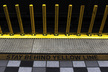 Stay behind the yellow line. Metro warning markings and yellow safety poles on the metro platform. The subway platform.