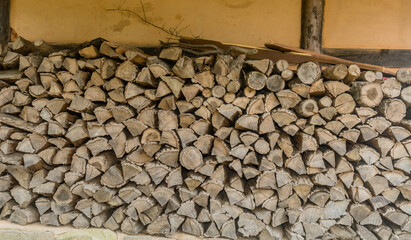 Firewood logs stacked neatly next to exterior wall.