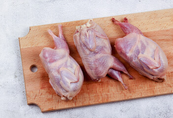 Raw quails on a wooden cutting board on a light gray background. Top view, flat lay