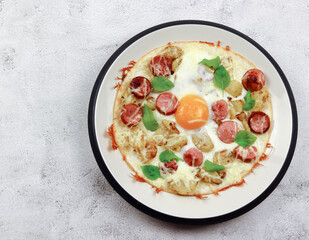 Tortilla with cheese, potatoes, sausages and fried egg on a round plate on a light gray background. Top view, flat lay
