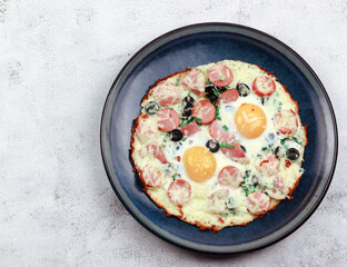 Fried eggs with green onions, cheese, sausages and olives on a round plate on a light gray background. Top view, flat lay