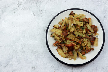 Fried potatoes with meat and mushrooms on a round plate on a light gray background. Top view, flat lay
