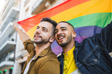 Gay couple embracing and showing their love with rainbow flag.