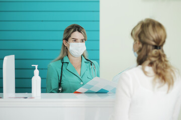 Woman doctor or nurse in a medical mask talks to a female patient