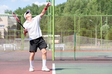 An elderly man plays tennis on an outdoor court