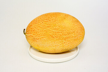 Yellow melon on white plate on light background close up