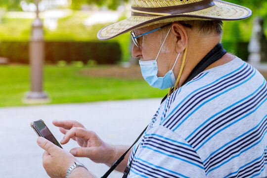 Portrait of an old man a wearing medical mask with using smartphone while listening protect during coronavirus in a park