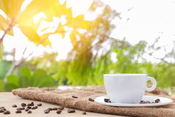 White hot coffee cup with coasters and coffee beans placed on brown burlap cloth on a natural background.
