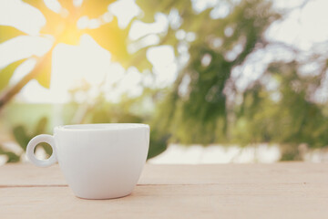 A white hot coffee cup is placed on a wooden plate and on the landscape nature background.