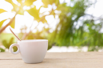 A white hot coffee cup with spoon in a cup is placed on a wooden plate and on the landscape nature background.