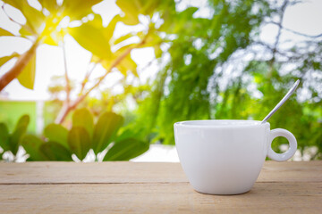 A white hot coffee cup with spoon is placed on a wooden plate and on the landscape nature background.