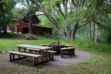 Naklejka premium Fireplace with benches and table. Sweden, Motala, Staffanstorp. Traditional red barn in the background