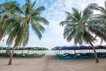 Empty beach chairs and colorful umbrella on tropical beach. The impact of the COVID-19 or coronavirus pandemic on the travel and hospitality industries.