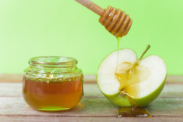 Jewish holiday, Apple Rosh Hashanah, on the photo have honey in jar and drop honey on green apples on wooden with green background