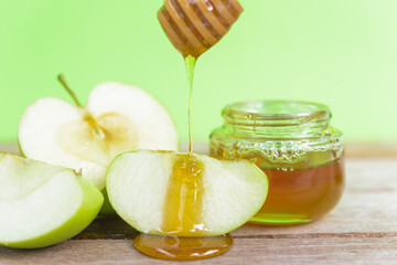 Jewish holiday, Apple Rosh Hashanah, on the photo have honey in jar and drop honey on green apples on wooden with green background