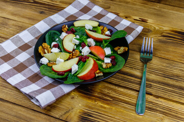 Autumn spinach salad with apple, feta cheese, walnut and dried cranberry on wooden table. Healthy vegetarian food