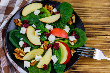 Autumn spinach salad with apple, feta cheese, walnut and dried cranberry on wooden table. Top view. Healthy vegetarian food