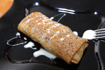 Delicious pancakes filled by fruits on black plate closeup