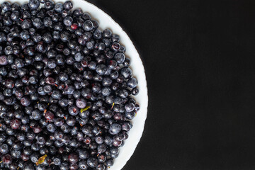 Blueberries in a white plate on a black background. Top view. Selective focus.