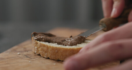 man spreading nut butter on ciabatta slice on olive board