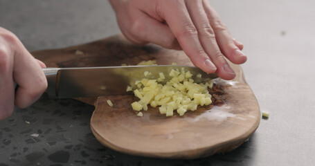 man hands chopping fresh ginger root with knife on olive wood board