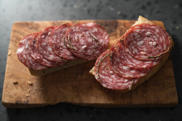 Ciabatta slices with slices of salami sausage on olive wood board