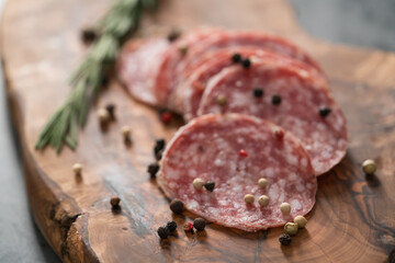 Sliced salame milano sausage on olive wood board with rosemary and pepper