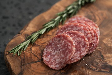 Sliced salame milano sausage on olive wood board with rosemary
