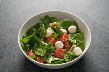 Salad with cherry tomatoes, spinach leaves and mozzarella balls in white bowl on terrazzo surface