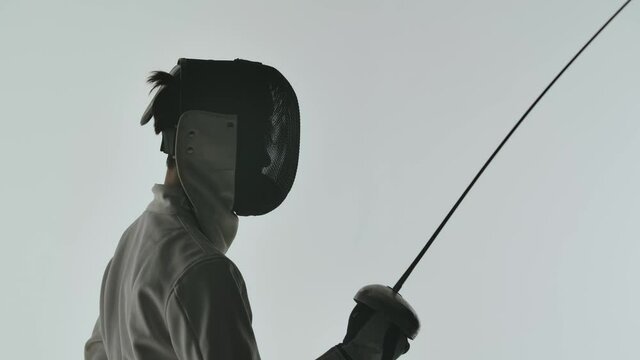 A close up swordsman in a helmet raises his saber up. Shot isolated on white background. Slow motion.