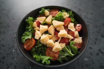 Salad with cherry tomatoes, kale and cheese in black bowl on concrete background