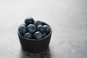 Fresh ripe blueberries in small black bowl on concrete background with copy space