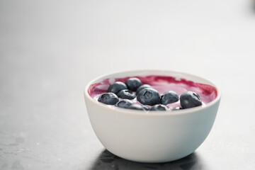 Blueberry yogurt with whole berries in white bowl on concrete background