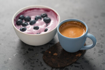 Blueberry yogurt with whole berries and cup of fresh espresso on concrete background
