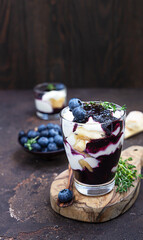 Dessert from mascarpone or ricotta cheese, blueberries and biscuit in glass on a dark background. No baked cheesecake or tiramisu.