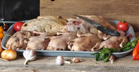 The process of processing wild ducks for cooking. Raw wild duck carcasses in a tray with ingredients for cooking on the background of a kitchen cutting board and oven.