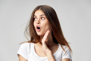 Woman with open mouth looking to the side hand near face white t-shirt studio 