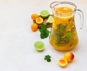 Apricot cocktail or ice tea with fresh mint, lime and apricots. Summer refreshing cold drink. Light concrete background.