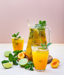 Apricot cocktail or ice tea with fresh mint, lime and apricots. Summer refreshing cold drink. Light concrete background.