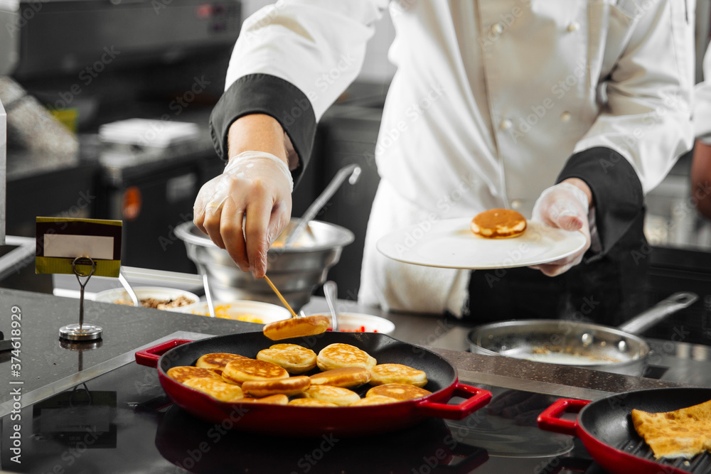 Wall mural chef puts pancakes on a plate from pan in kitchen